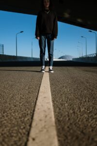 person in black pants and white sneakers standing on gray asphalt road