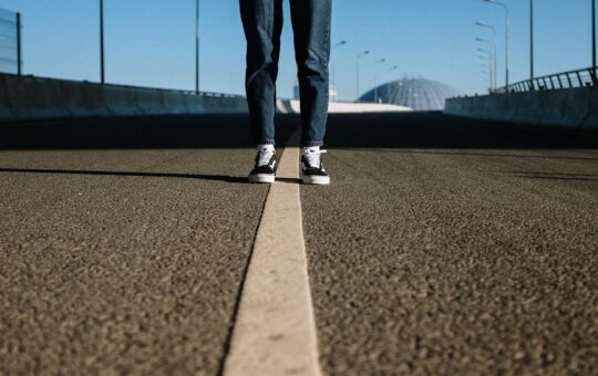 person in black pants and white sneakers standing on gray asphalt road