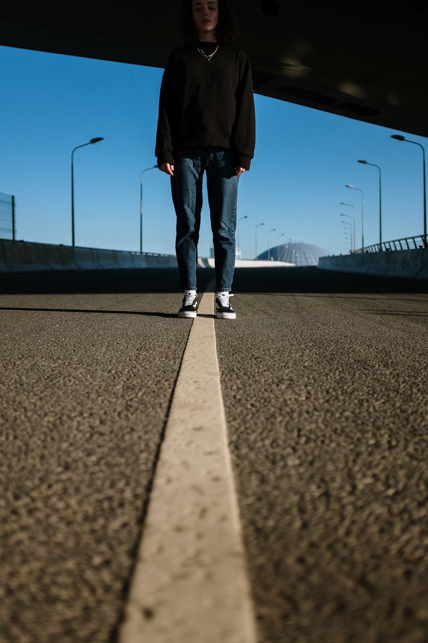 person in black pants and white sneakers standing on gray asphalt road