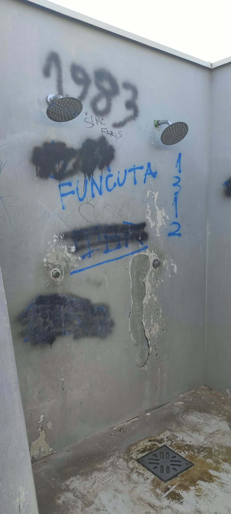 Zid vanjskog tuša s dvije tuš-glave, prekriven grafitima, oljuštenom bojom i mrljama