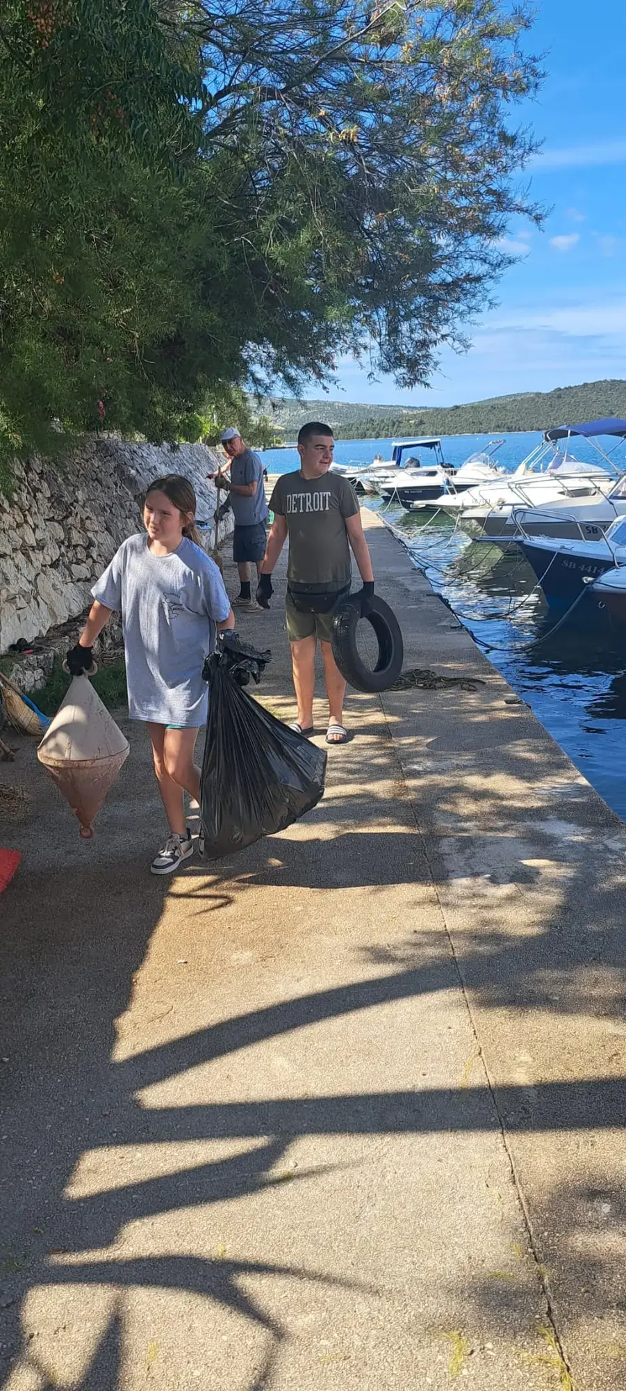 Mladi volonteri nose vreće s prikupljenim otpadom uz rivu