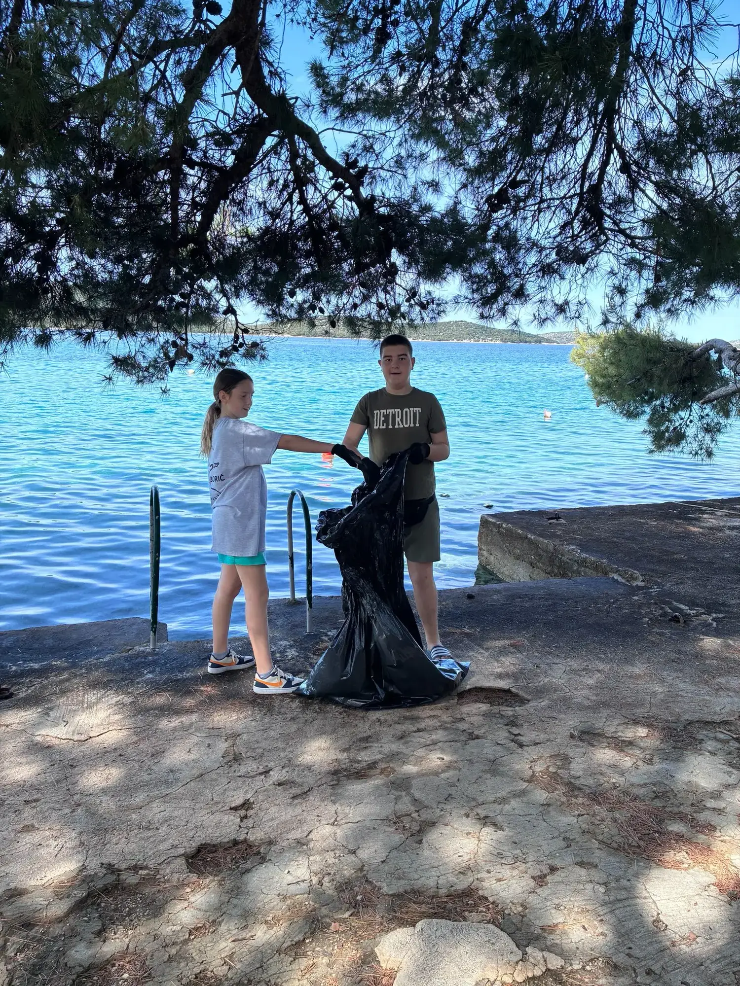 Dvoje učenika puni vreću otpadom uz more
