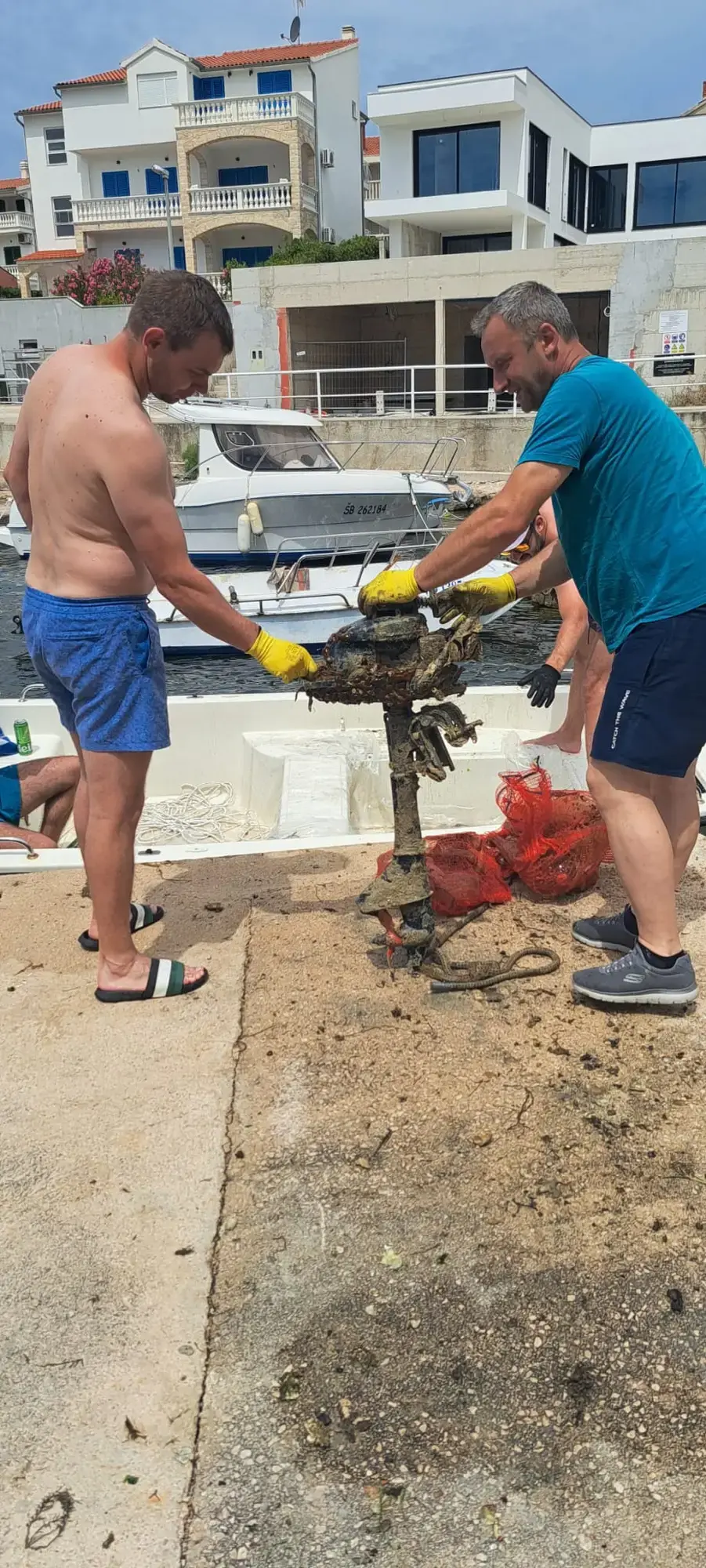 Dva volontera iznose obrasli vanbrodski motor izvučen iz mora