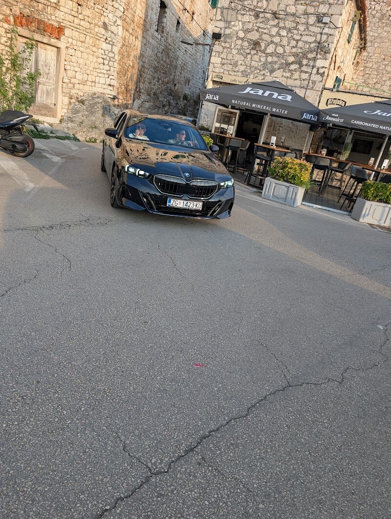 Automobil prolazi uskom ulicom u Docu tik uz štekat kafića