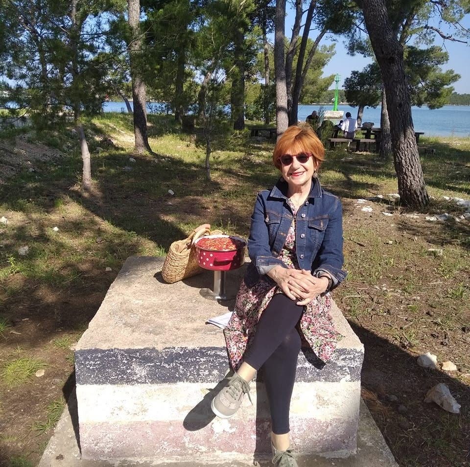 Živana Podrug sjedi na kamenoj klupi u borovoj šumi uz more