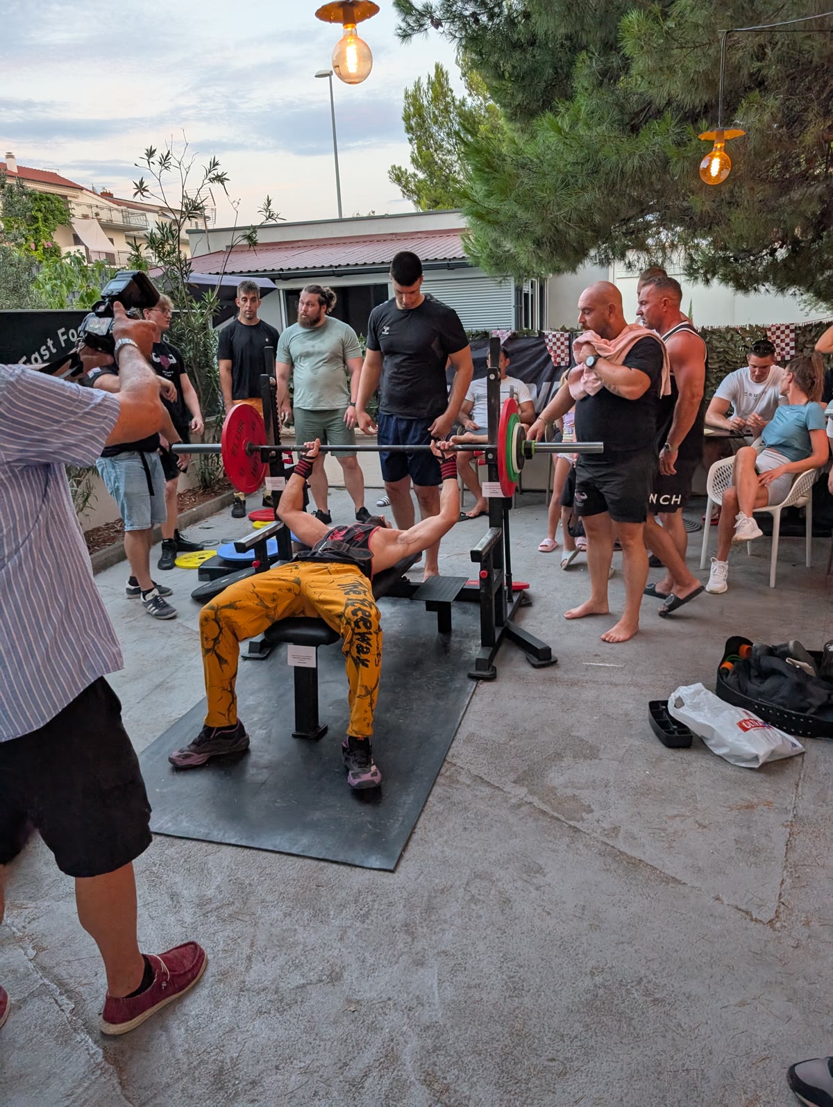Natjecatelj izvodi bench press dok ga osiguravaju spotteri, publika promatra